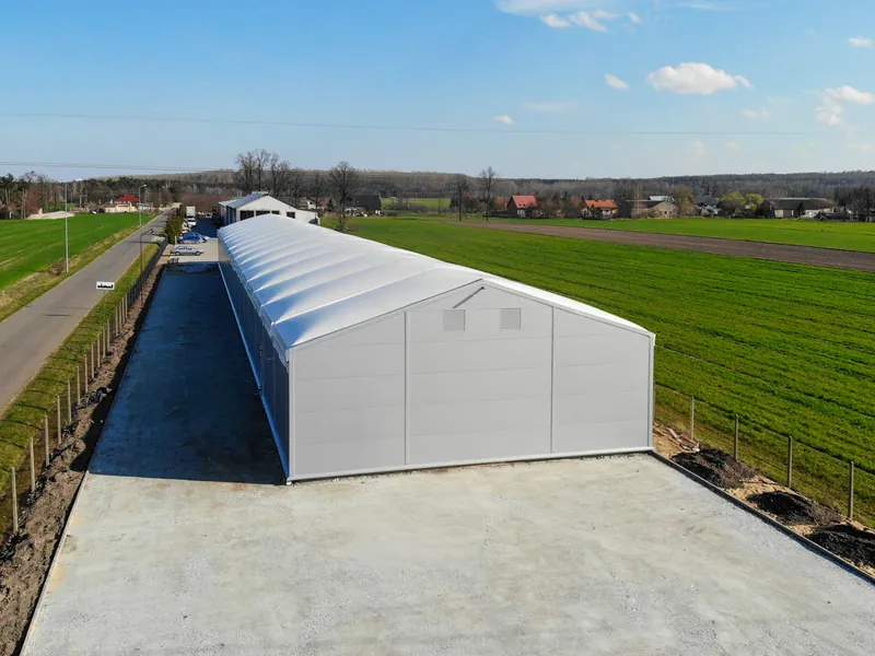 White steel-framed temporary building with a PVC roof, standing in open countryside